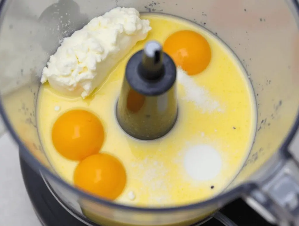 Imagen en primer plano de la Thermomix mezclando huevos, queso crema, azúcar y leche para hacer flan de queso.