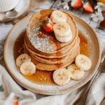 Tortitas de avena y plátano con rodajas de banana y fresa, bañadas en jarabe.